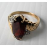 A 9ct yellow gold marquise-cut garnet ring with diamond accents in a cage setting, size M,