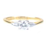 A diamond three stone ring The round brilliant-cut diamond flanked by tapered baguette-cut