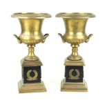 A pair of reproduction brass pedestal urns on stands Each with wreath decoration to lower bodies,