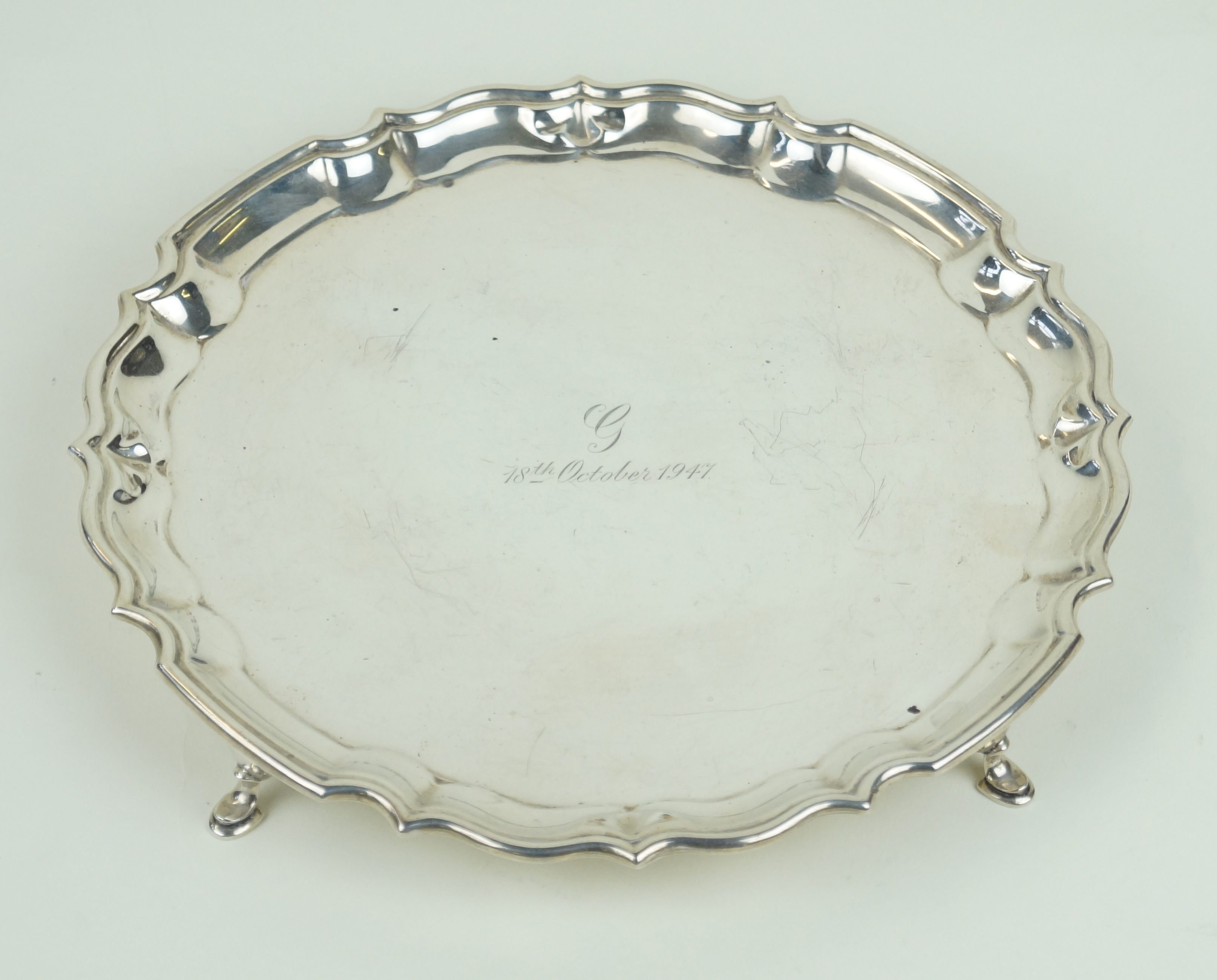 A George V hallmarked silver card tray With cast rim, raised on three hoof feet,