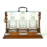 An early 20th Century oak framed three bottle Tantalus Having silver-plated and chrome mounts,
