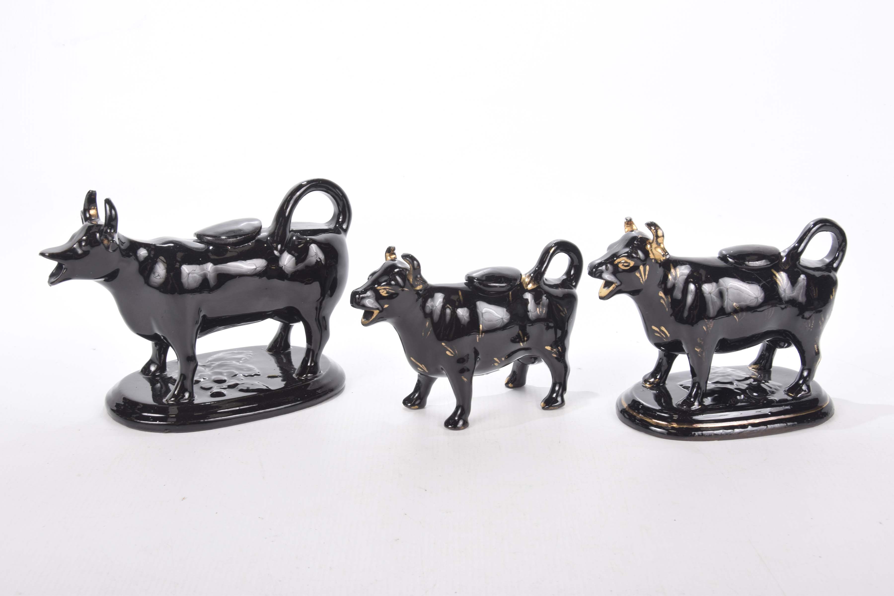 Three black Staffordshire cow creamers, late 19th, early 20th century Two with gilt decoration,