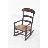A 19th Century stained hardwood child's rush seat rocking chair With a ladder back above an