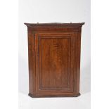 A George III oak and mahogany crossbanded hanging corner cupboard With a moulded cornice above a