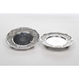 A pair of silver dishes The scalloped circular dish with scrolling chased foliate designs,