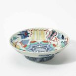 A Japanese Nabeshima dishRaised on a high foot and decorated in tones of underglaze blue, red,