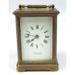 A circa 1900 French brass carriage clock with swing loop handle above rectangular white enamel dial