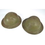 Two British WWI period green painted Brodie type helmets both with textured finish with internal