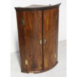 A late George III mahogany two-door wall-hanging bow-fronted corner cupboard with H-shaped brass