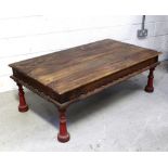 An Indian hardwood rectangular coffee table with carved frieze and turned red painted supports,