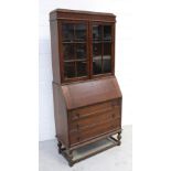 A mid-20th century oak bureau bookcase, twin glazed doors above drop-down desktop,