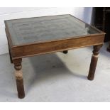 An Indian hardwood table with glass top over an antique window frame insert with metal decoration