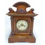 An oak mantel clock with shaped pediment above circular dial set with Arabic numerals flanked by