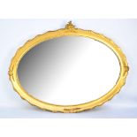 A gilt framed oval bevelled wall mirror with rococo style ornaments to the top, 65 x 86.5cm (af).