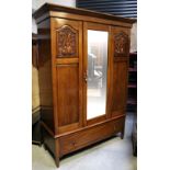 A walnut wardrobe with single mirror door flanked by carved foliate scroll detail above single long