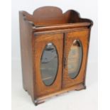 An Edwardian oak smokers' cabinet with pair of glazed door enclosing three drawers, a tobacco