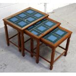 A nest of three teak tables with blue and green tiled tops on square legs to splayed feet,