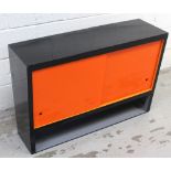 A retro c1950s wall-hanging kitchen cabinet with sliding orange Perspex doors above lower shelf,