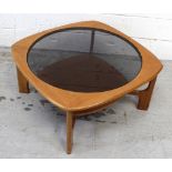 A retro teak coffee table with smoked glass top and lower shelf on spreading supports,