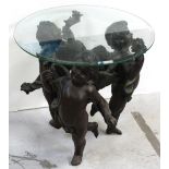 A decorative circular glass-topped side table supported by three composite bronzed putti figures,