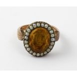 A yellow metal dress ring with central oval amber coloured stone and seed pear surround, size M,