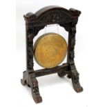 A Burmese brass gong mounted in oak frame profusely carved with foliate detail with scrolled feet