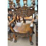 An ornate X-framed open arm elbow chair with carved mask detail.