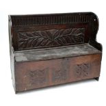 An oak settle with carved foliate decoration to back and hinged seat above further carved detail,