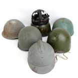 Six WWII period and later helmets in green and blue including American examples and a helmet liner.