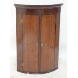 A George III oak and mahogany crossbanded bowfronted hanging corner cupboard, width 73cm.