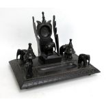 A carved ebony desk stand with ink well, pen rest and watch stand,