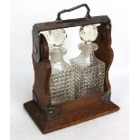 An early 20th century silver plated oak miniature tantalus with two square sectioned glass