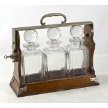 An Edwardian oak and silver plate mounted Betjemann's patent tantalus with three clear glass