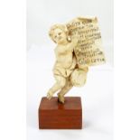 A 19th century carved ivory figure of a cherub holding aloft the Epistle of Paul to the Colossians