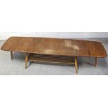 An Ercol drop leaf coffee table in golden stain supported on turned beech legs with magazine shelf