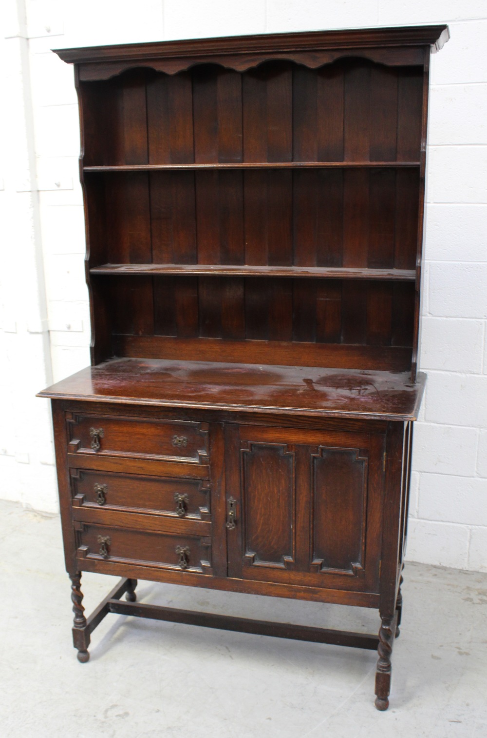 A 1920s oak dresser with boarded plate rack raised on barleytwist supports, width 107cm.