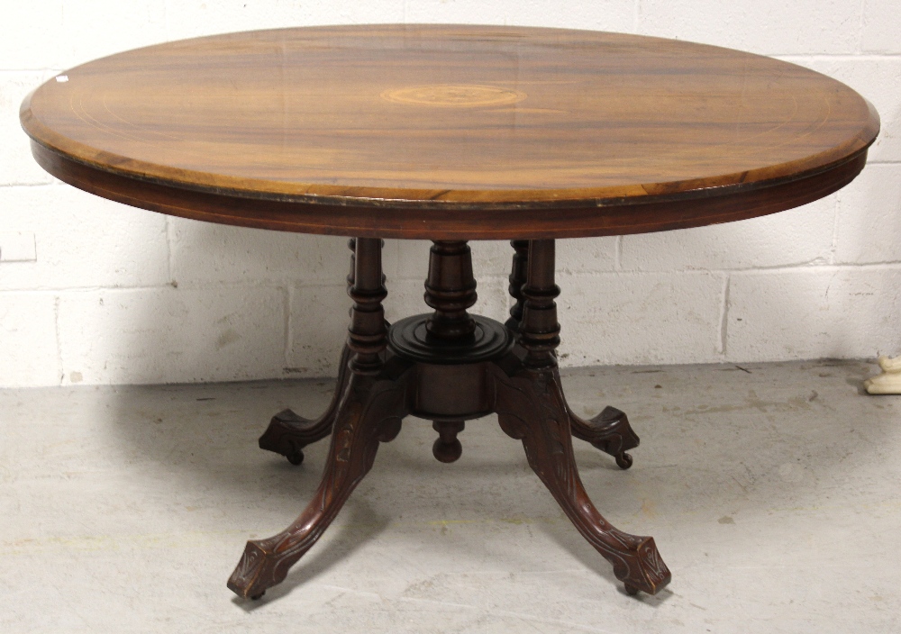 A Victorian walnut and inlaid loo table raised on carved quadripartite base to castors,