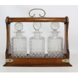 An early 20th century oak and silver plate mounted three bottle tantalus with hobnail cut glass