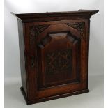 A wooden table top cabinet, the single door with carved detail enclosing arrangement of shelves,