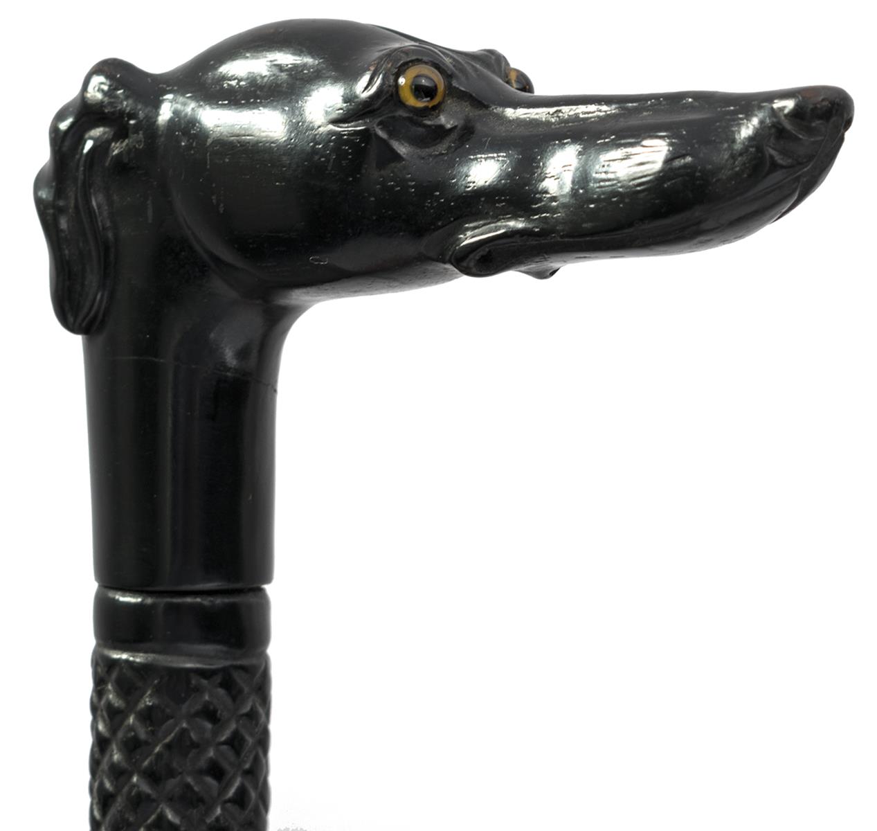 A CARVED EBONY WALKING STICK, the grip carved as a greyhound's head with inset glass eyes, the shaft