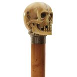 A LATE 19TH CENTURY WALKING CANE, the ivory pommel carved as a skull with a snake curled around