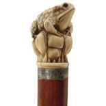 AN EARLY 20TH CENTURY WALKING CANE, the pommel carved as a frog sitting on rocks, above white