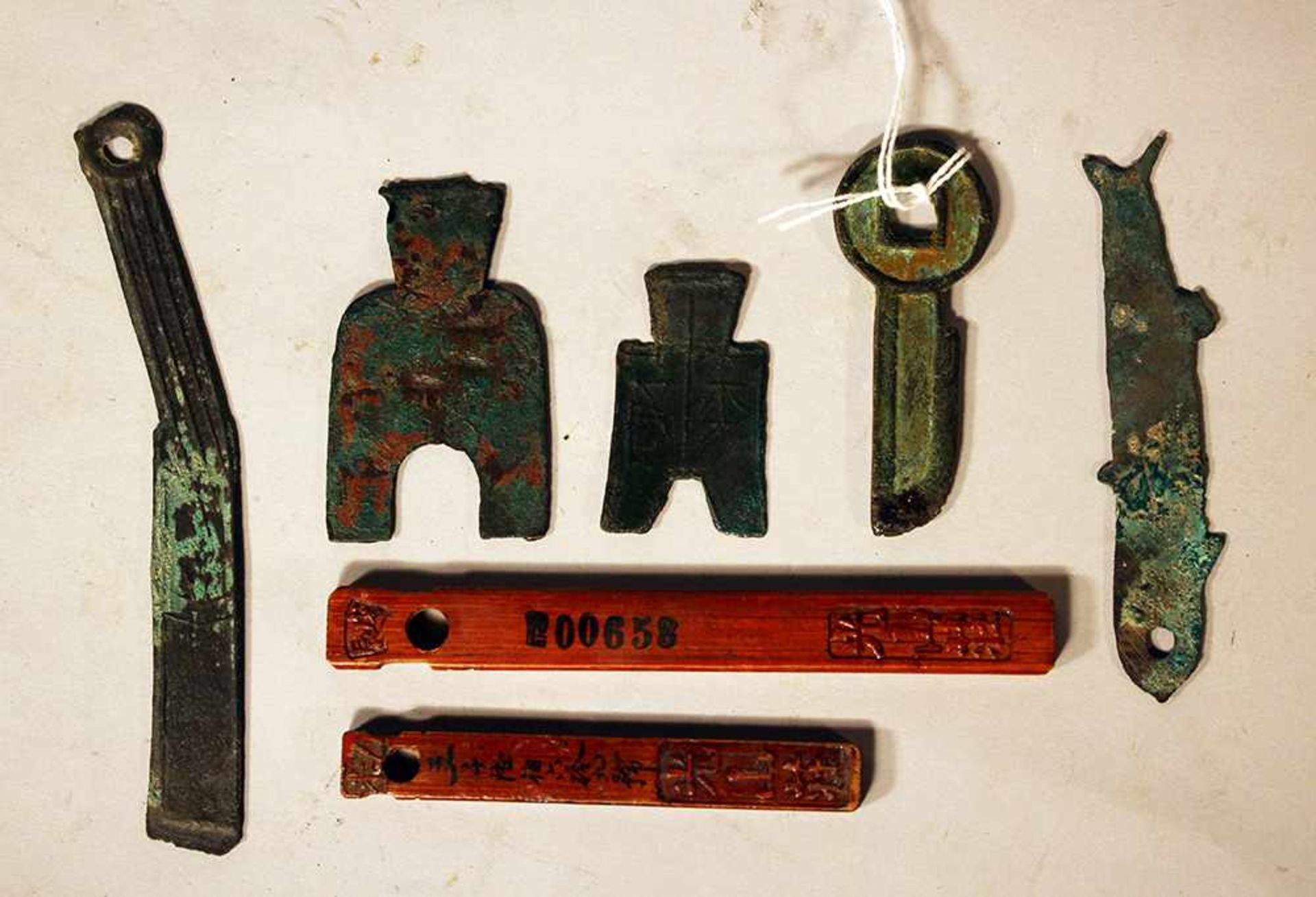 Lot of seven Asian wooden and bronze money symbols; partly with script signs and verdigris; seven