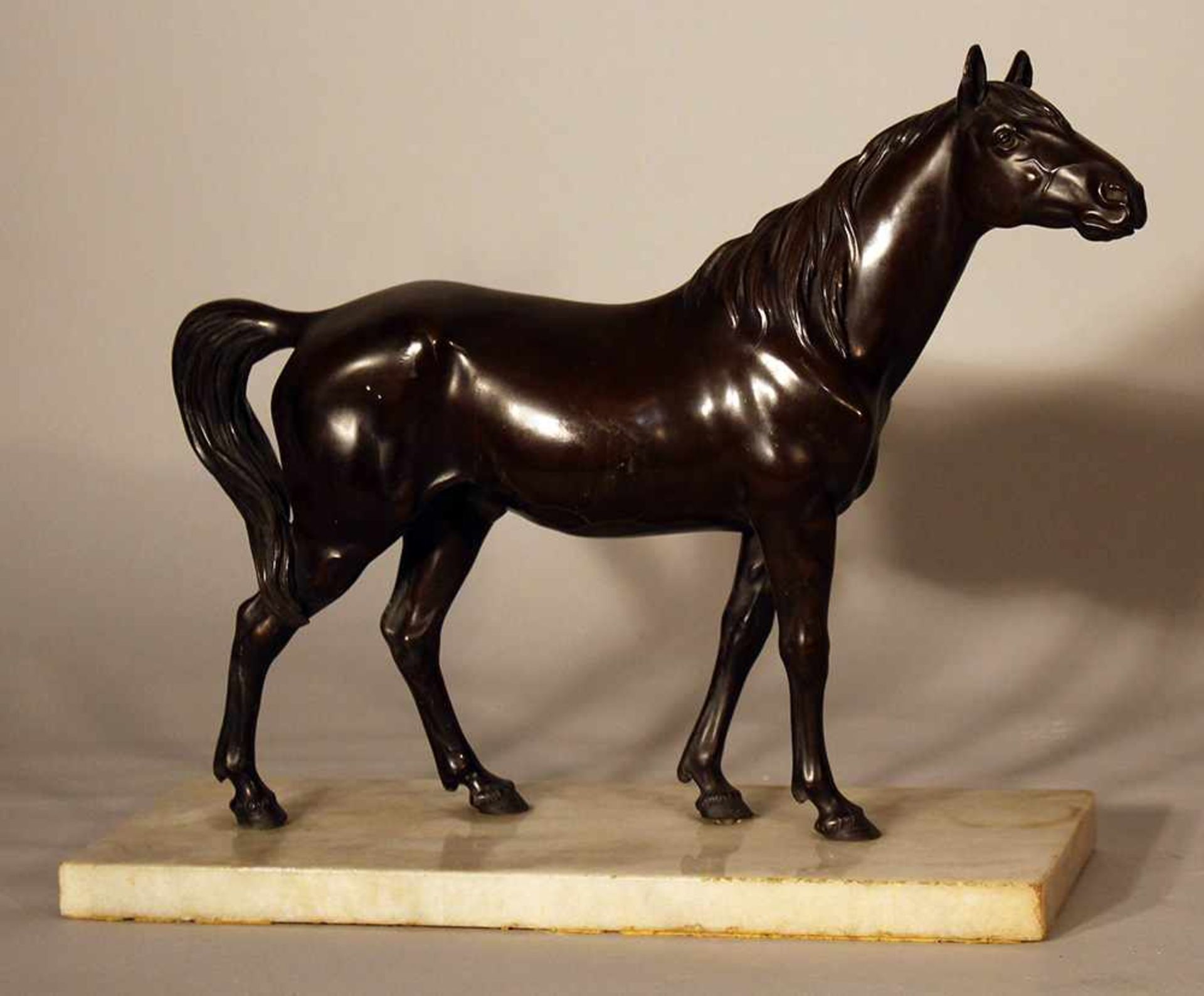 Bronze sculpture of a standing horse looking to the side, on white marble base; bronze cast with