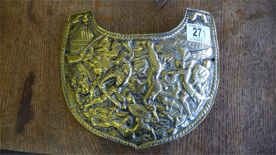 A brass shield shaped chest plate, decorated in the classical style with warriors fighting