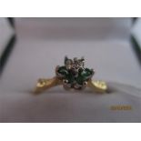 An 18ct gold ring set with emeralds around a central diamond in a floral style setting