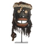 A traditional polychrome decorated African wooden mask with fiber, cowrie snails and fur, Guere -