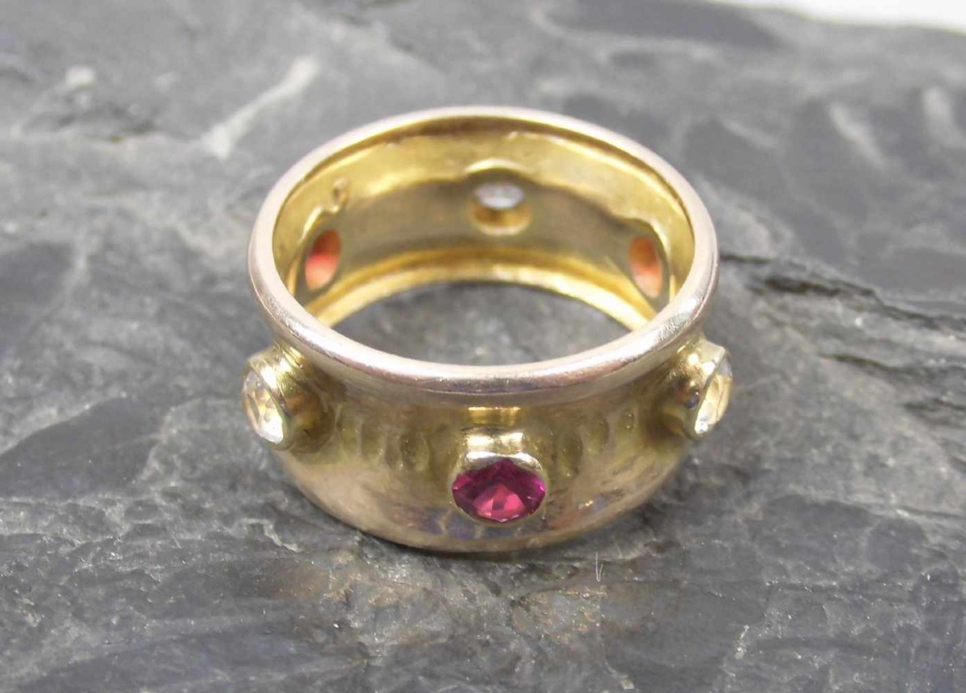 RING, 333er Gelbgold (getestet, 5,8 g), breite Ringschiene besetzt mit Rubinen und weißen Safiren.