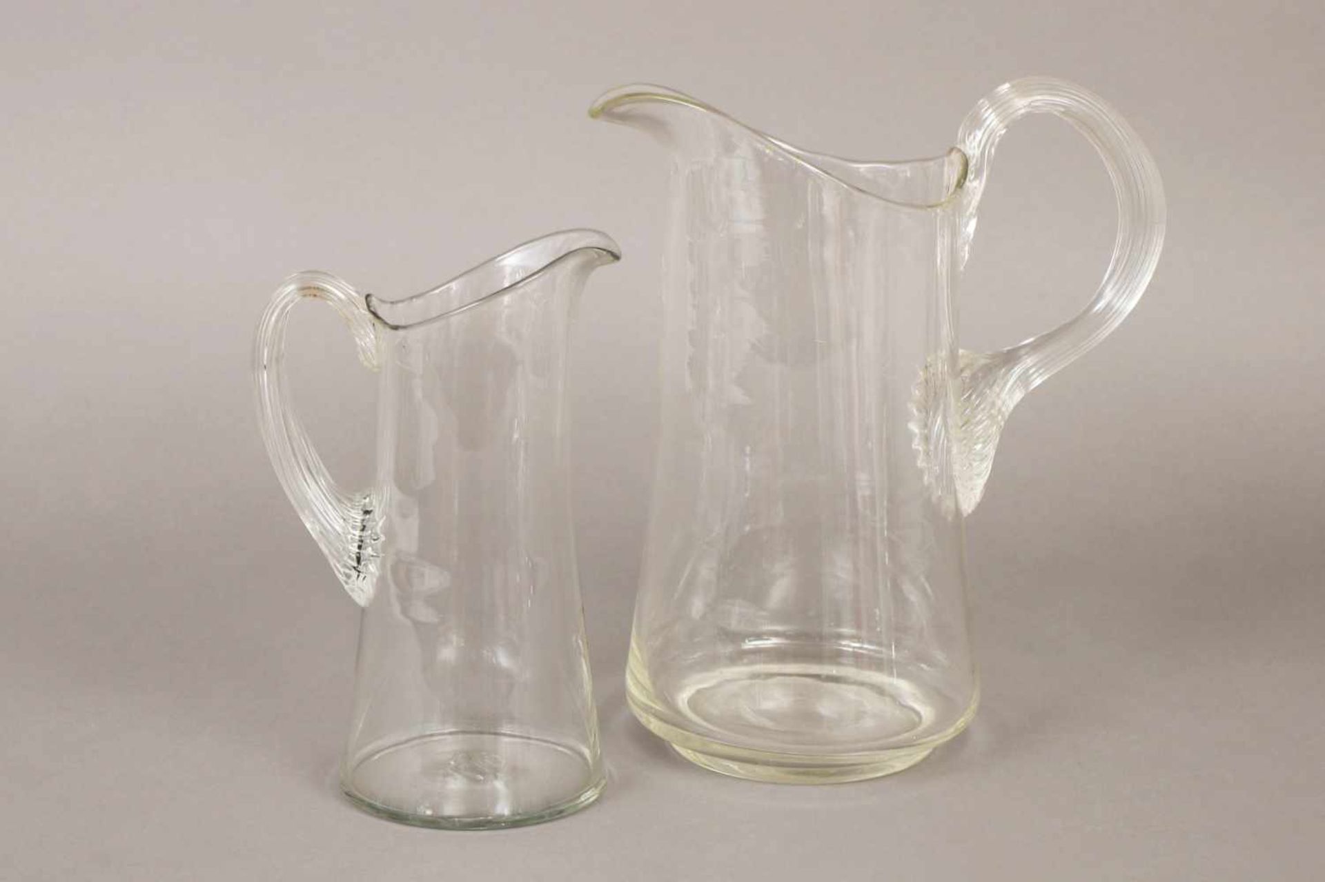 Paar Glaskrügefarbloses Glas, konischer Korpus mit breitem Ausguss, ohrenförmiger Henkel, gerippt, H