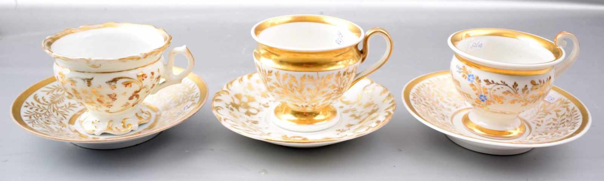 Drei Tassen mit Untertasse, aufwendig mit goldenen Ranken und Ornamenten verziert, eine Tasse mit
